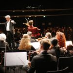 Dirigent leitet Orchester vor Publikum im Konzertsaal